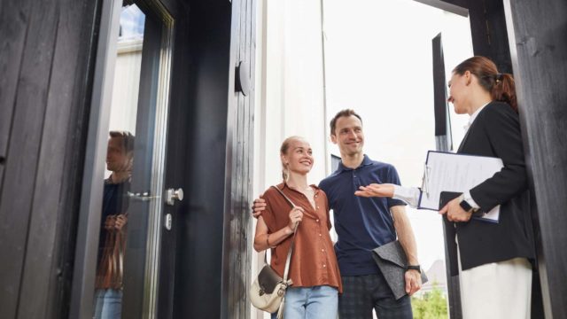 Immobilienmaklerin, die ein junges Paar trifft, das beim Kauf eines neuen Hauses in der Tür steht