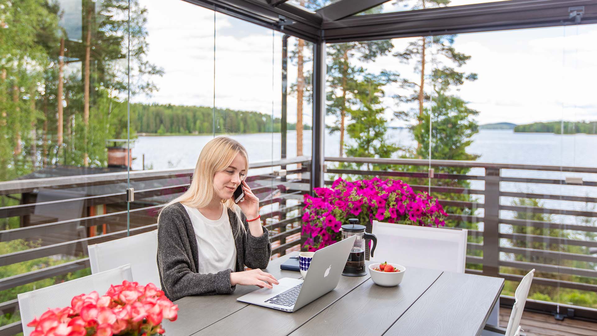Femme assise devant son ordinateur portable et téléphonant avec son portable sur une terrasse vitrée