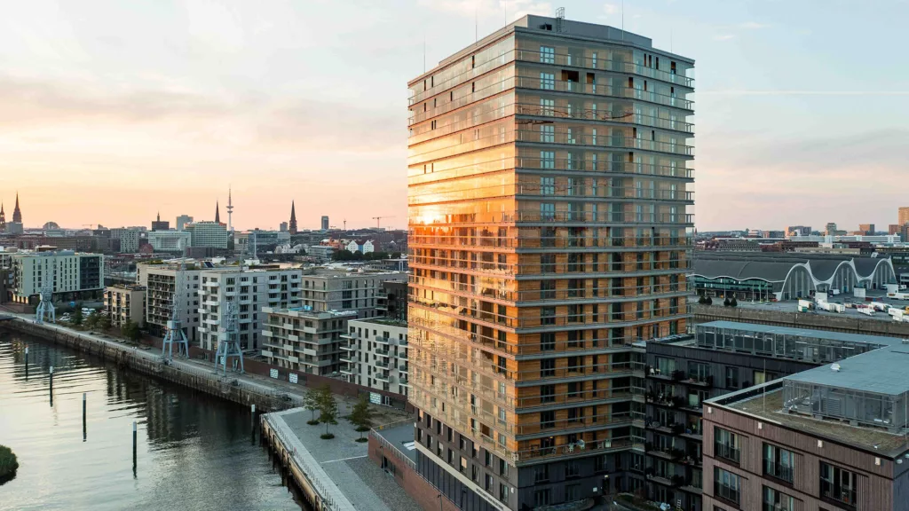 Blick in die Ferne über Häuser an der Elbe. Im Vordergrund das Holzhochhaus roots mit Balkonverglasungen.