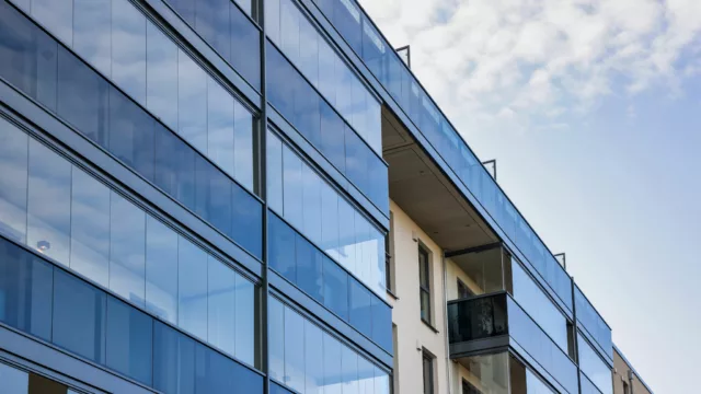 Blick von unten auf ein Haus mit einer Glasfassade aus Balkonverglasung und Ganzglasgeländer. Die Geländer sind braun.