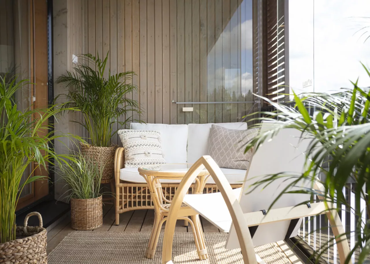 Balkon mit vielen grünen Topfpflanzen einer Sitzecke aus Holzmöbeln und einer Balkonverglasung