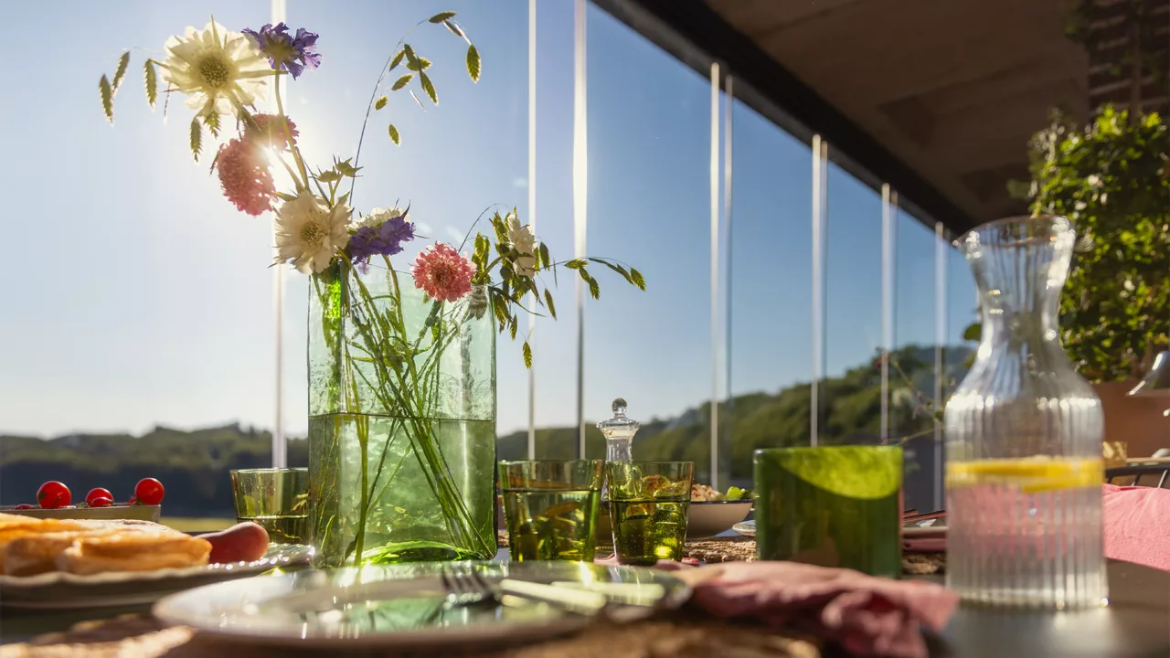 Gedeckter Tisch auf einem verglasten Balkon mit einer Vase und Frühlingsblumen im Vordergrund