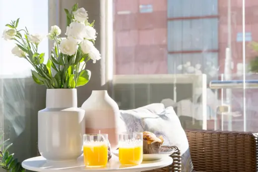 Auf einem verglasten Balkon steht ein Rattansessel mit einem gedeckten Beistelltisch.