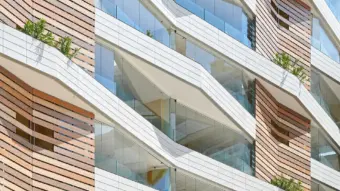 Blick von unten auf eine Fassade mit Holzverkleidung und verglasten Balkonen.