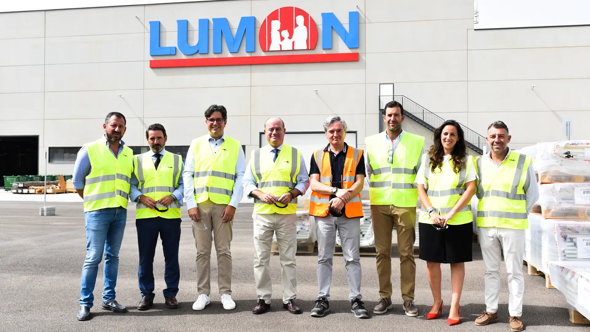 Sieben Personen mit Warnweste stehen vor einer Fabrik mit Lumon-Logo