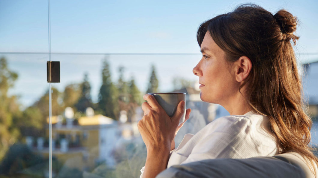 Frau sitzt auf Balkon mit Balkonverglasung und trinkt ihren Kaffee