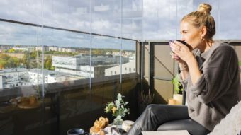 Eine Frau genießt ihren Kaffee auf einem verglasten Balkon.