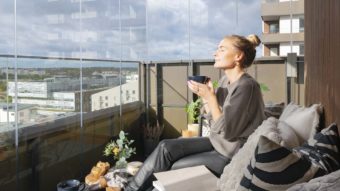 Frau genießt ihren Kaffee auf einem verglasten Balkon