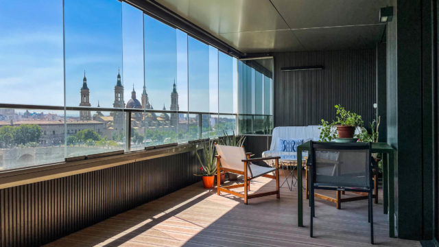 Loggia mit Balkonverglasung als Schiebe-Dreh-System. Auf der Loggia befindet sich ein Tisch mit Stühlen, eine Couch und mehrere Topfpflanzen.