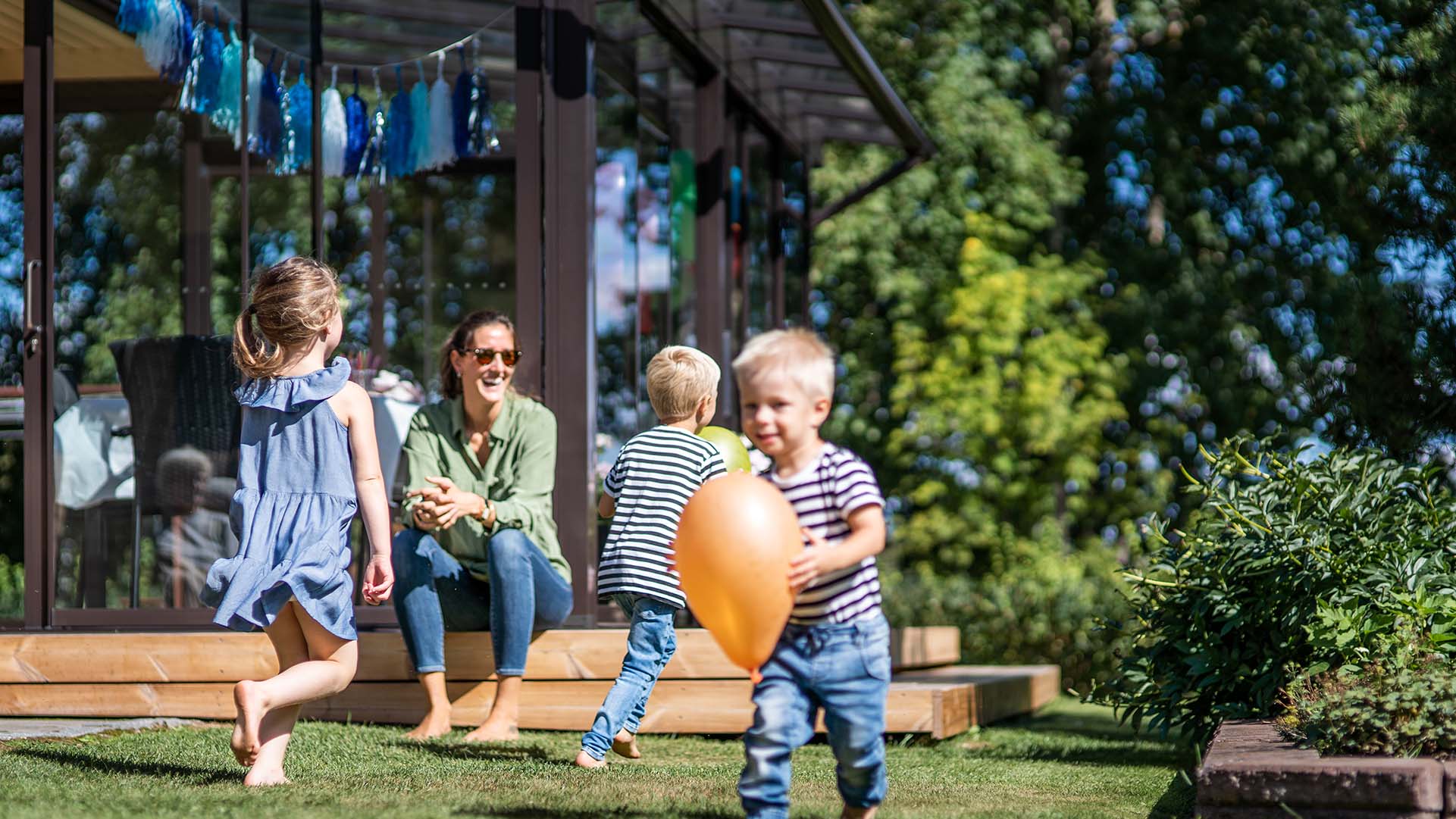 Kinder spielen im Garten vor einer verglasten Terrasse.