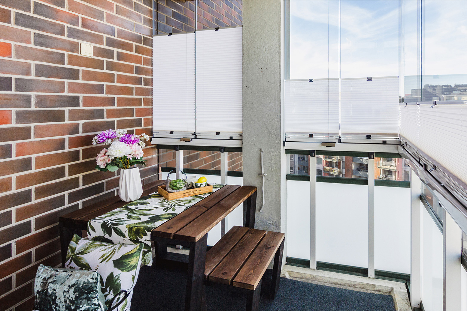 Verglaster Balkon mit Tisch, Bank und Plissees