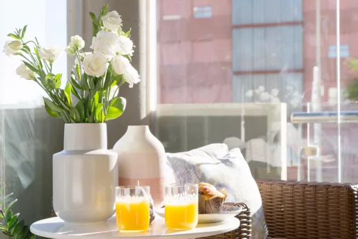 Auf einem verglasten Balkon steht ein Rattansessel mit einem gedeckten Beistelltisch.