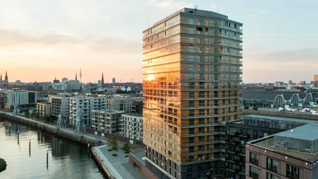 Blick in die Ferne über Häuser an der Elbe. Im Vordergrund das Holzhochhaus roots mit Balkonverglasungen.