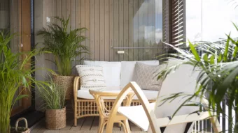 Balkon mit vielen grünen Topfpflanzen einer Sitzecke aus Holzmöbeln und einer Balkonverglasung