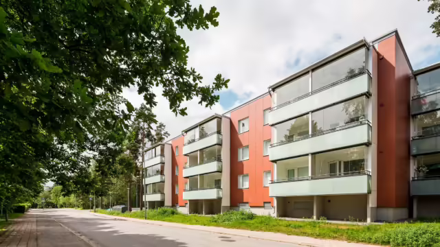 Blick auf mehrere Balkone mit Verglasung nach durchgeführter Balkonsanierung. Die Balkone haben eine Glasfassade aus Glasgeländer und Balkonverglasung. Der Putz des Hauses ist rot.