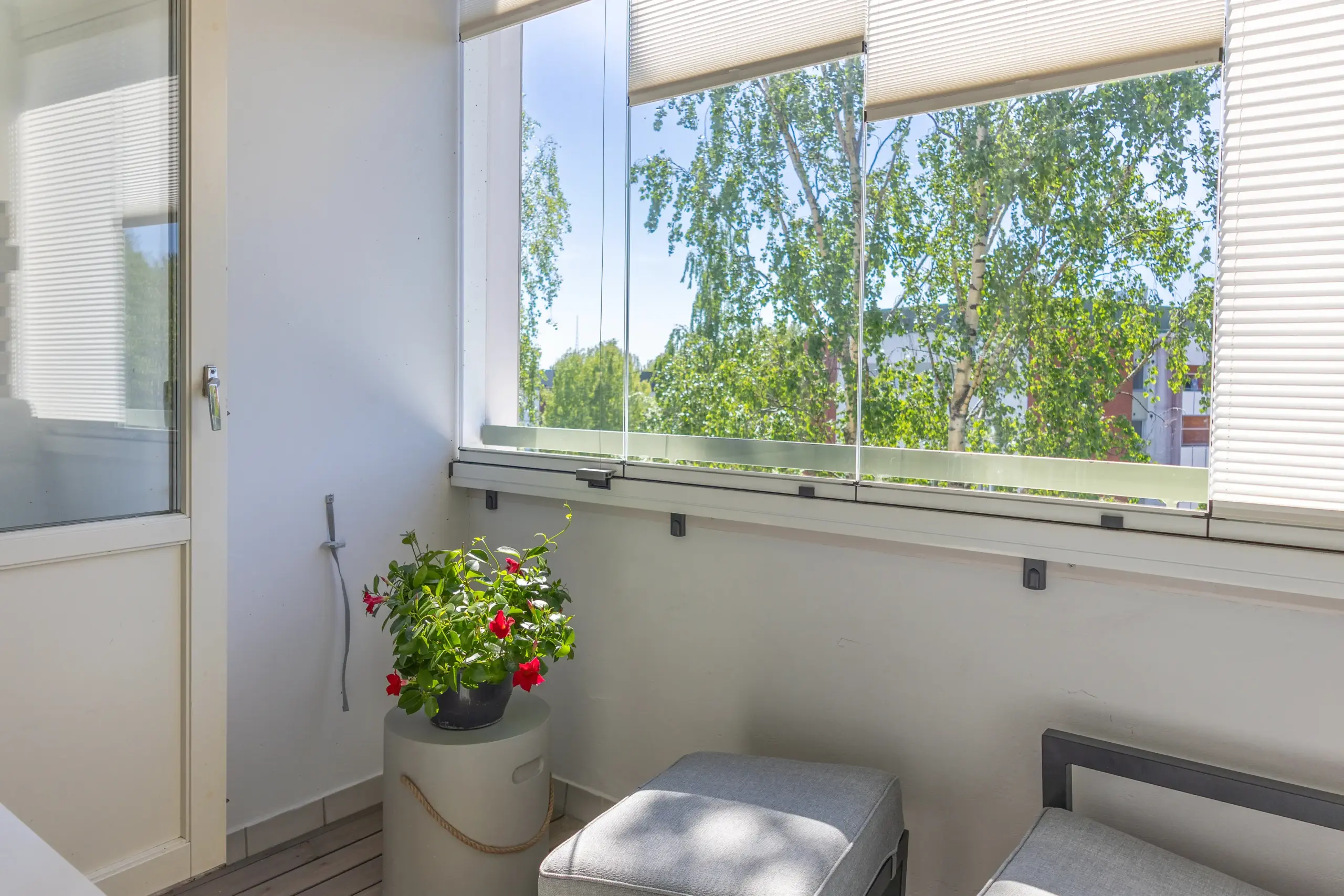Die Möbel auf einem Balkon sind durch eine Verglasung geschützt. Die Plissees bieten Sonnenschutz
