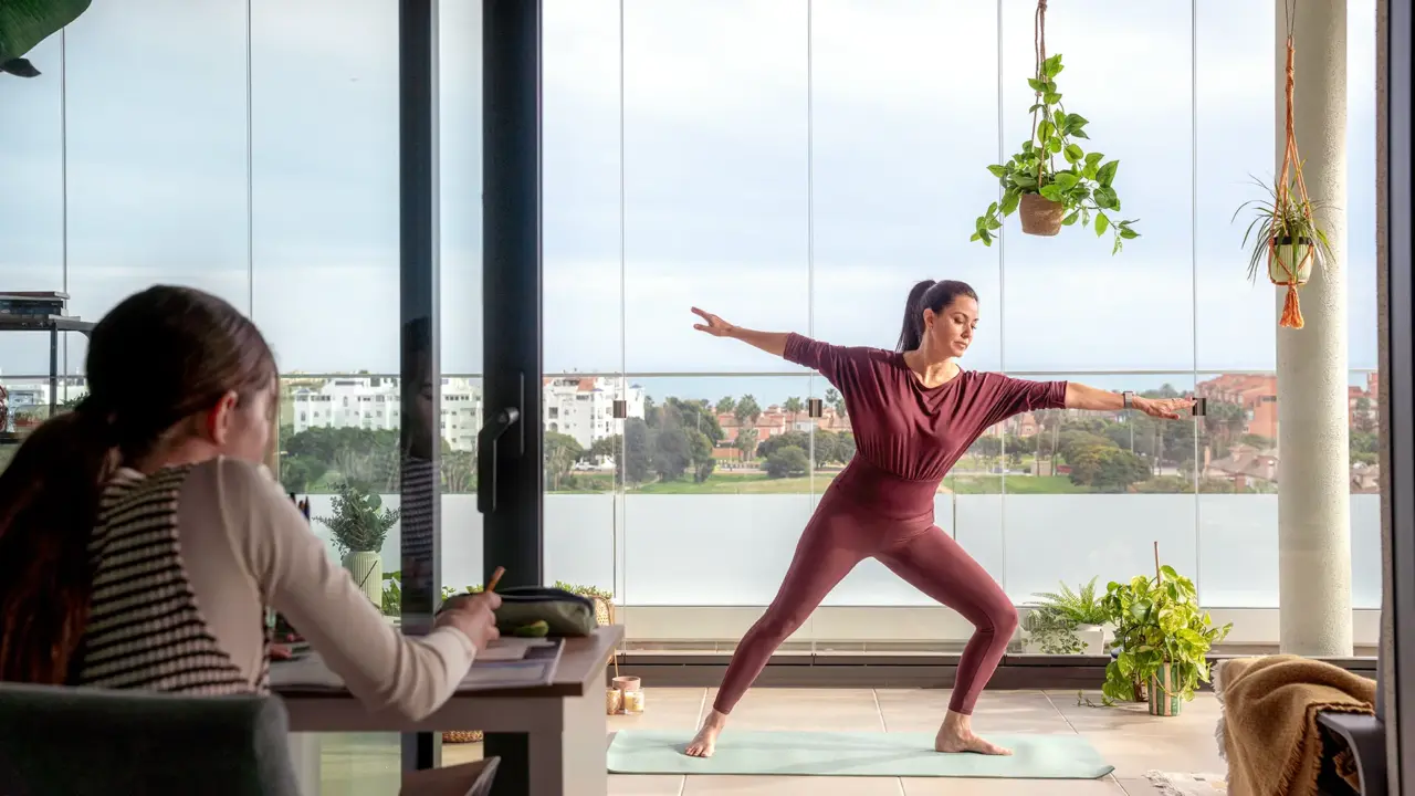 Eine Frau macht Yoga auf ihrem verglasten Balkon