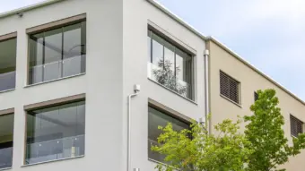 Teil eines weißen Mehrfamilienhauses mit verglasten Balkonen