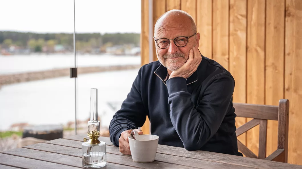 Tommy Hellsten istumassa lasitetulla terassilla kahvikuppi kädessä