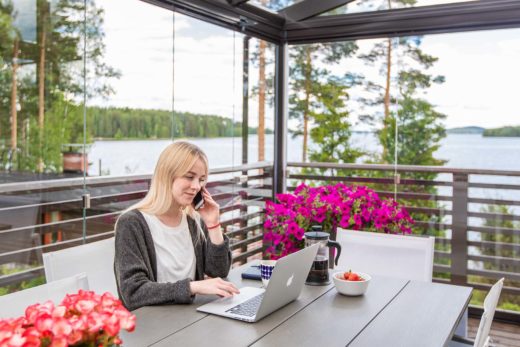 Femme assise devant son ordinateur portable et téléphonant avec son portable sur une terrasse vitrée